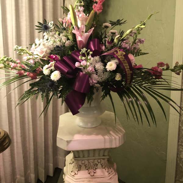 Large pink and white floral arrangement in a white vase with a purple ribbon