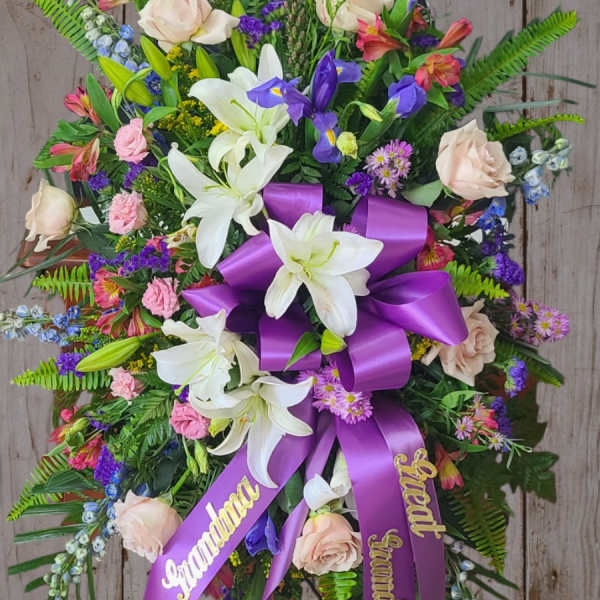Standing floral spray with white lilies, pale roses, and a purple ribbon bow