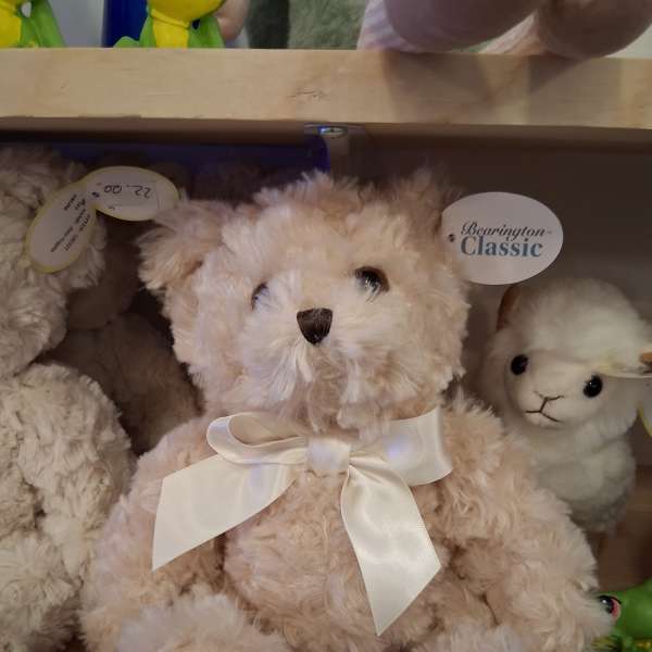 Plush teddy bear with a white ribbon bow sitting on a shelf