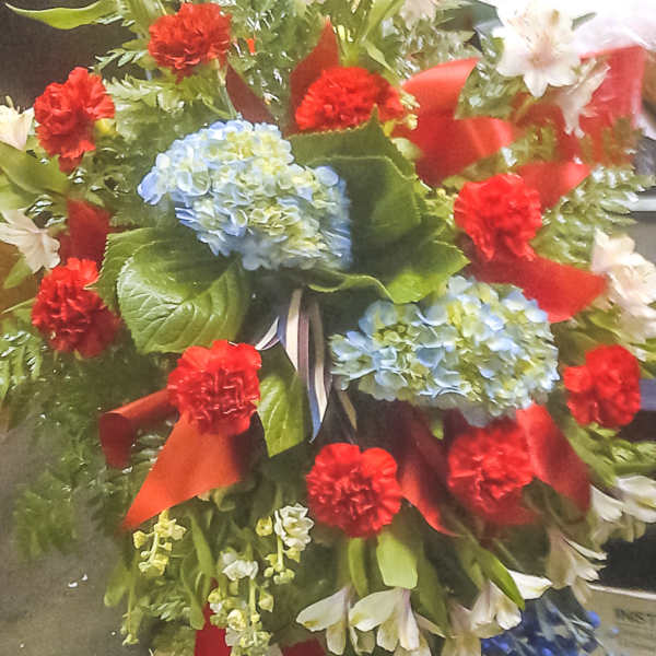 Large standing floral spray with red carnations, blue hydrangeas, and white lilies
