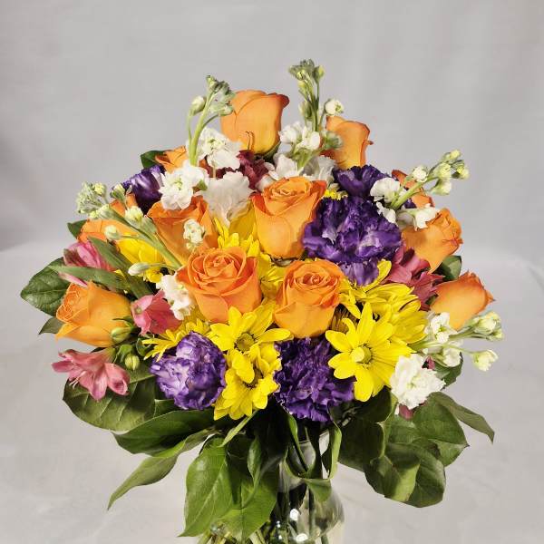 Mixed bouquet of orange roses, purple carnations, and yellow daisies in a glass vase