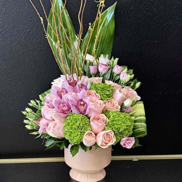 Pink roses and orchids in a pale pink vase with tall branches