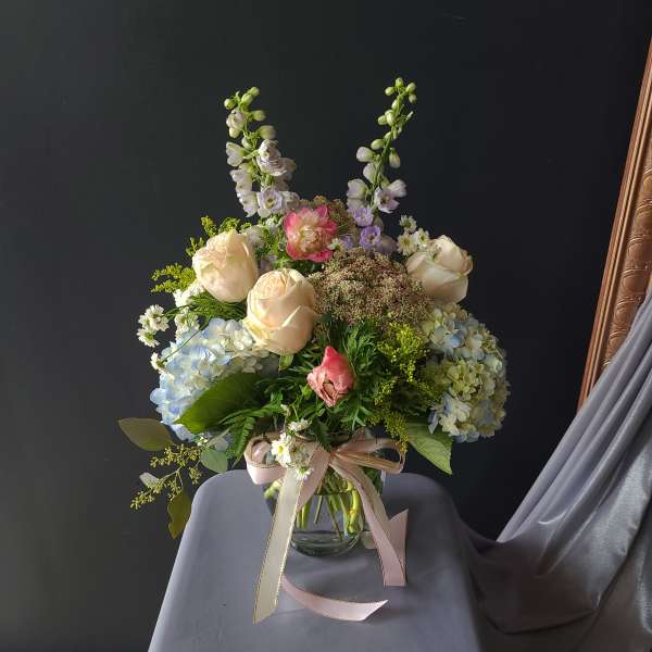 Pastel bouquet of roses, hydrangeas, and tall lavender blooms in a glass vase
