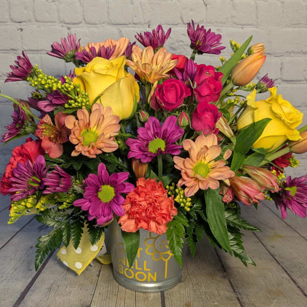 Colorful mixed bouquet in a metal container with yellow roses and purple daisies.