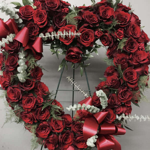 Heart-shaped wreath of red roses with ribbon bows on a stand