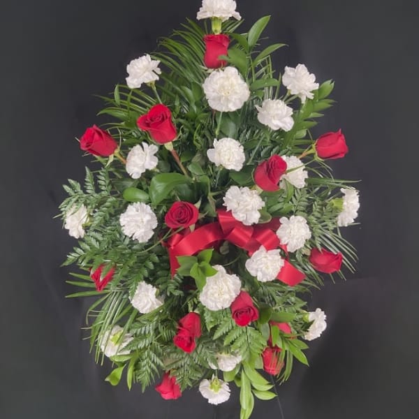 Red roses and white carnations in a standing spray with a red ribbon