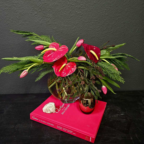 An arrangement of red anthuriums and pink tulips in a glass bowl vase