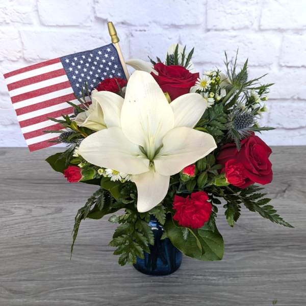 Red roses and white lilies in a blue vase with an American flag