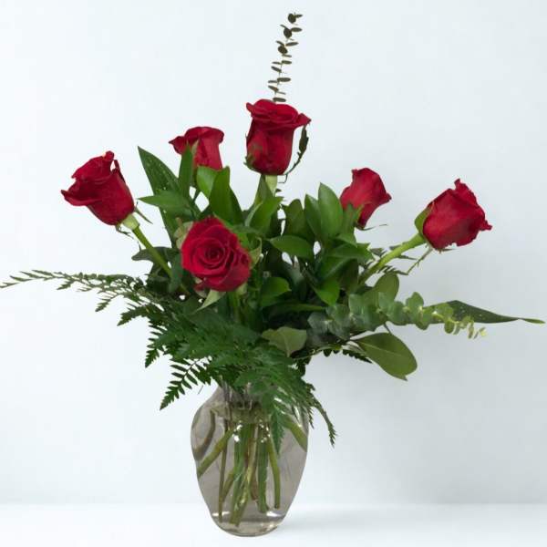 Red roses arranged in a clear glass vase with greenery