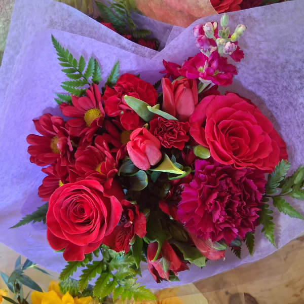 Bouquet of red roses, carnations, and daisies wrapped in lavender paper