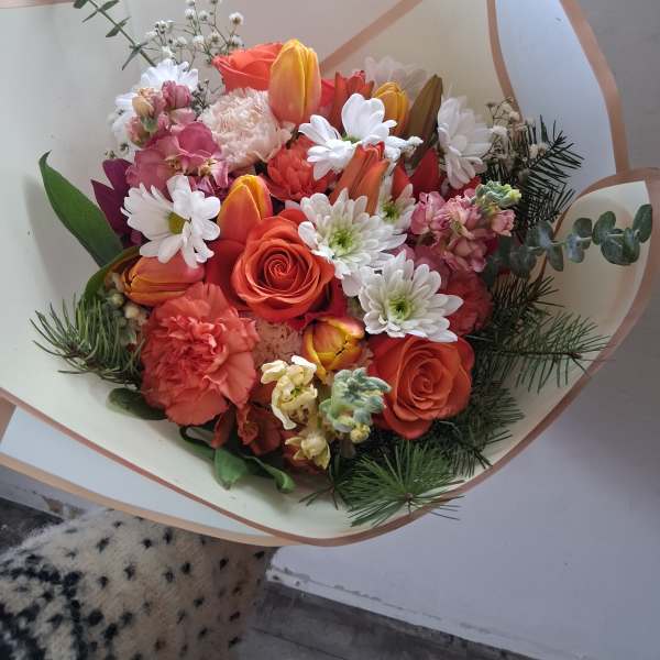 Bouquet of orange roses, tulips, and white daisies wrapped in cream paper