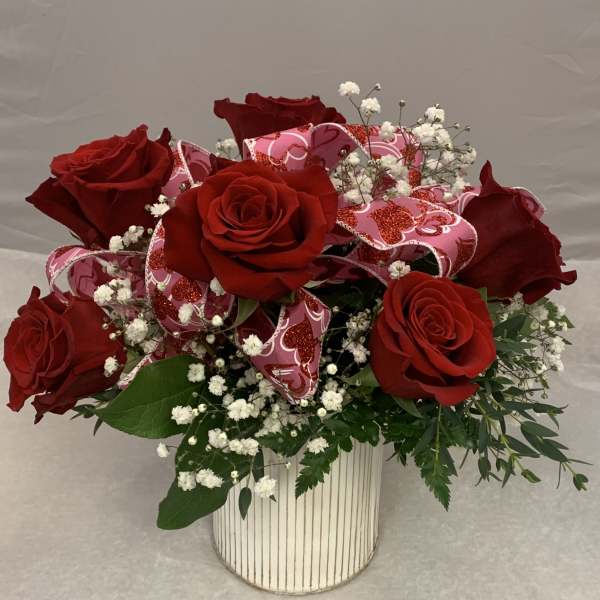 Red roses arranged in a striped white vase with pink ribbon and baby's breath