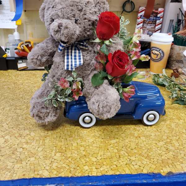 Teddy bear sitting on a toy car with red roses and pink flowers