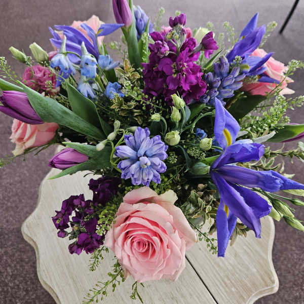 Colorful bouquet with pink roses, purple stock, tulips, blue iris and hyacinth on a light wood table