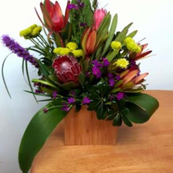 Tropical floral arrangement with purple spikes and red-orange blooms in a wooden box