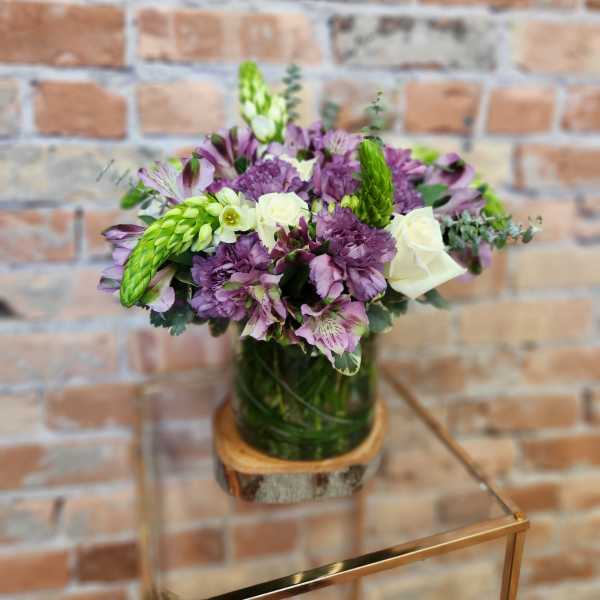 Purple and white bouquet in a glass vase on a wooden base