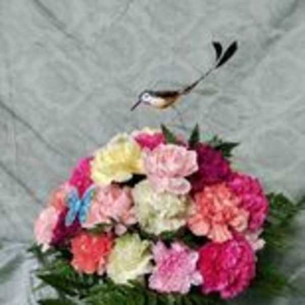 Colorful bouquet of carnations in a glass vase with a bird ornament above