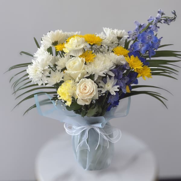 Bouquet of white and yellow flowers with blue blooms in a wrapped vase