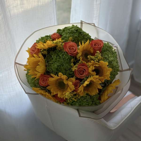 Bouquet of yellow sunflowers and coral roses wrapped in white paper