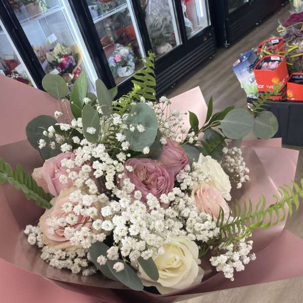 Handheld bouquet of pink and white roses with white filler flowers wrapped in pink paper.