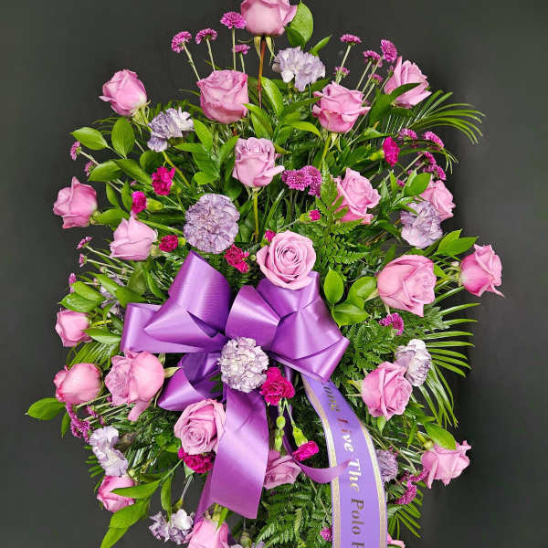 Pink rose and carnation funeral spray with a purple ribbon
