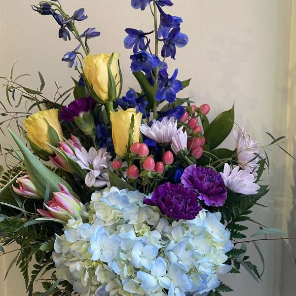 Tall mixed bouquet in a glass vase with blue, yellow, pink, and white flowers