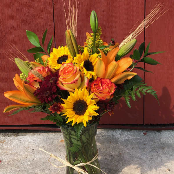 Bouquet of sunflowers, orange lilies, and roses in a glass vase