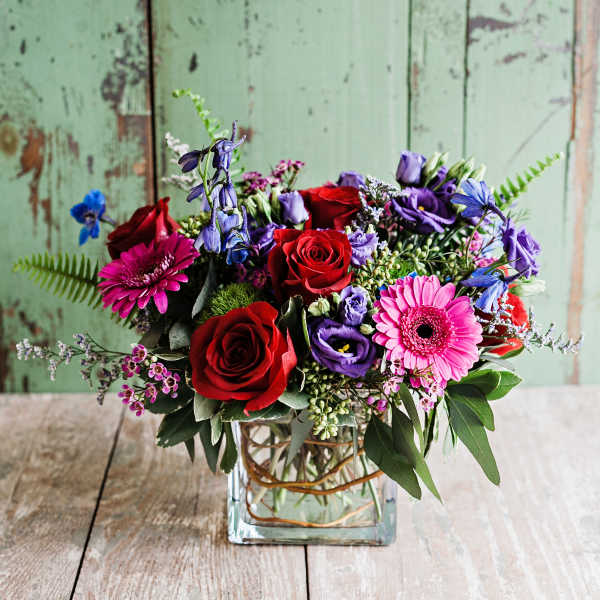 Mixed bouquet of red roses, pink gerberas, and purple flowers in a glass vase