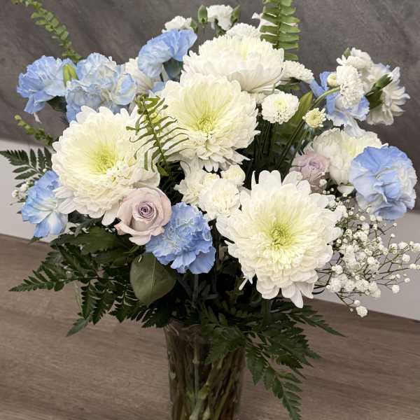 Tall vase arrangement of white mums, blue carnations, and pale roses with ferns.