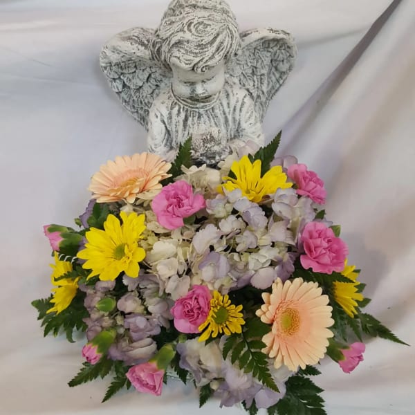 Angel figurine with low pastel flower arrangement of yellow daisies, pink blooms, and hydrangeas at the base.
