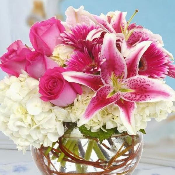 Pink roses and lilies arranged with white hydrangeas in a glass bowl vase