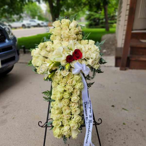 Cross-shaped floral spray of cream roses and white lilies with a ribbon