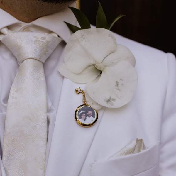 White orchid boutonniere on a white suit jacket with a photo charm
