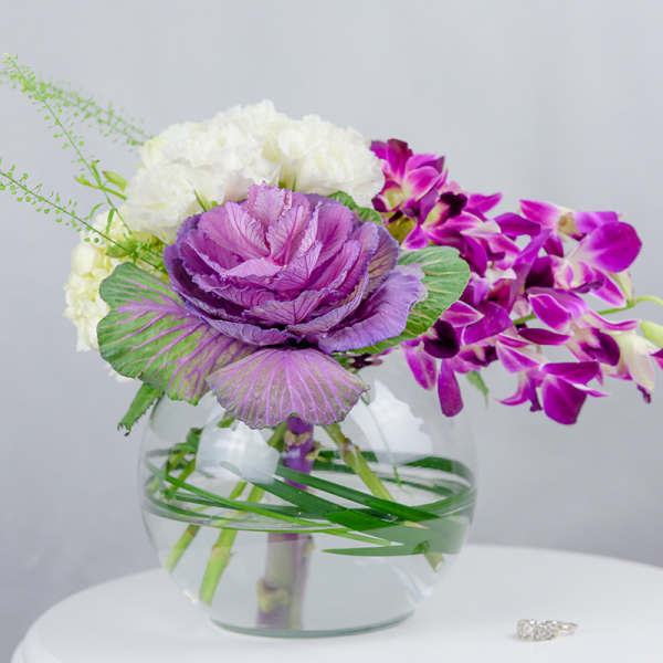 Purple and white floral arrangement in a clear glass bowl vase
