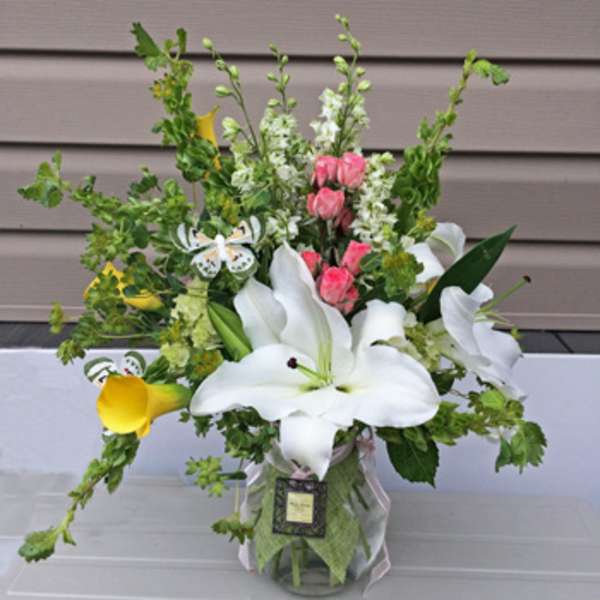 White lilies and pink flowers in a glass vase with greenery.