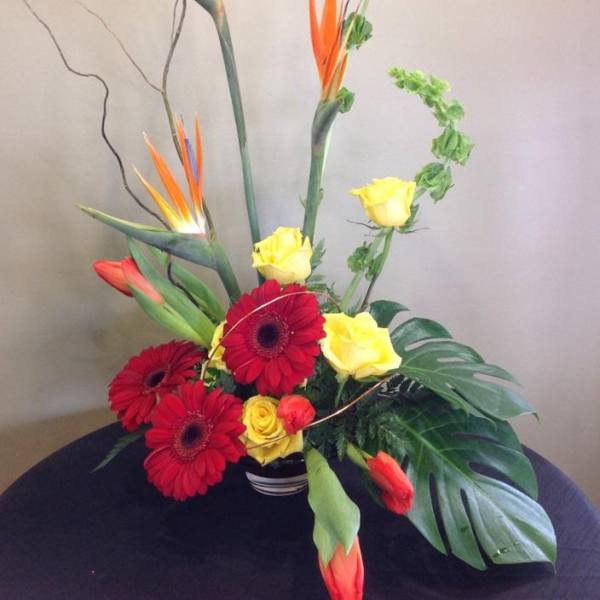 Tropical flower arrangement with red gerbera daisies and yellow roses in a vase