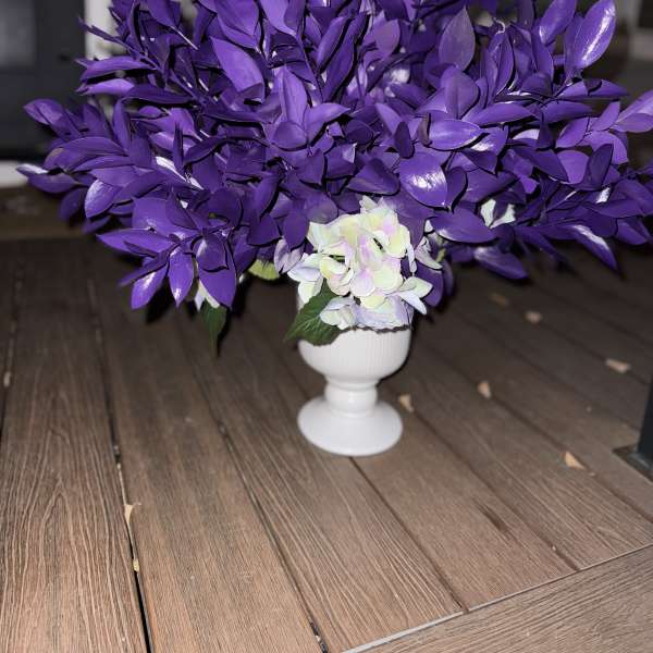 Purple floral arrangement in a white pedestal vase with pale blooms at the base