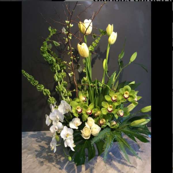 Tall floral arrangement with white orchids, cream roses, and yellow tulips