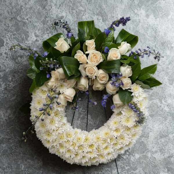 White floral wreath with cream roses and purple accents on a stand