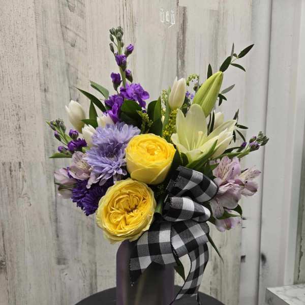 Bouquet of yellow and purple flowers in a purple vase with a black-and-white ribbon