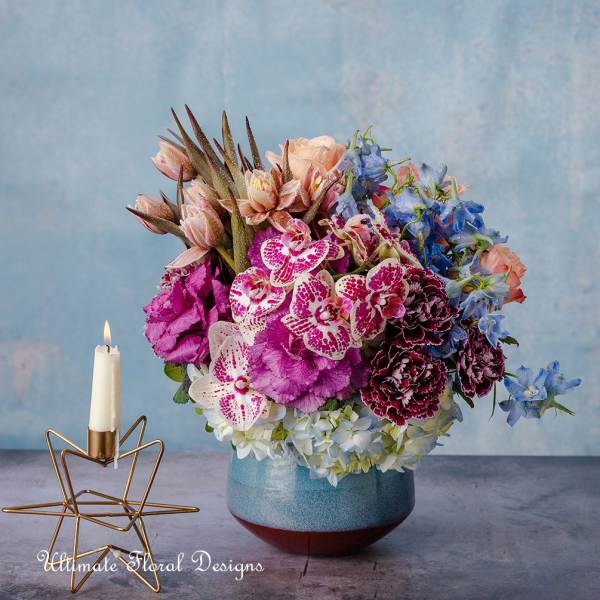 Colorful floral arrangement in a blue vase beside a lit candle holder