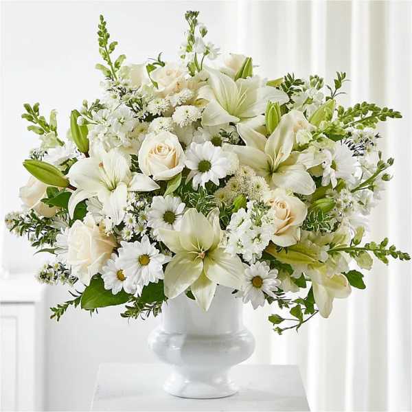 White floral arrangement in a white vase with lilies, roses, and daisies