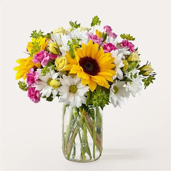 Bouquet of sunflowers, daisies, and pink carnations in a glass mason jar