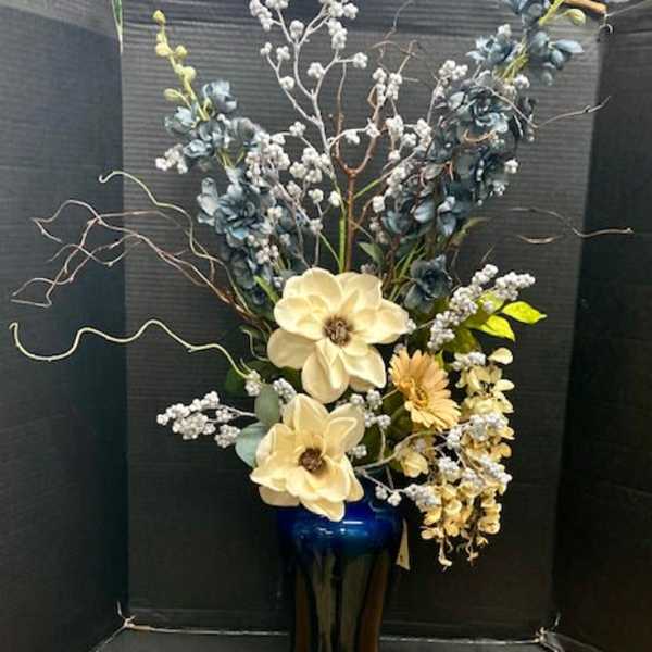 Tall floral arrangement in a blue vase with cream blooms and blue accents