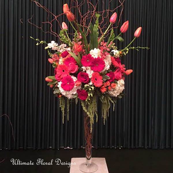 Tall floral arrangement with pink tulips and bright gerbera daisies in a glass vase