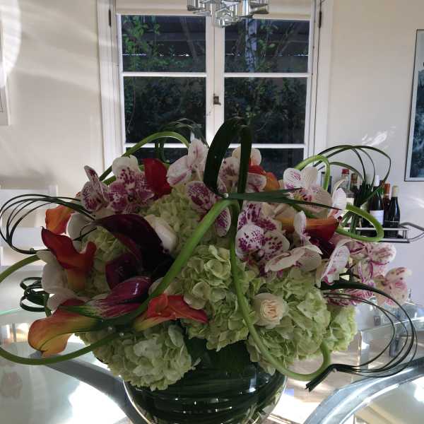 Large floral arrangement with orchids, hydrangeas, and calla lilies in a glass vase