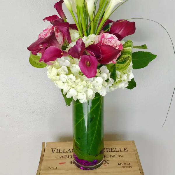 Pink and white calla lily arrangement in a tall glass vase