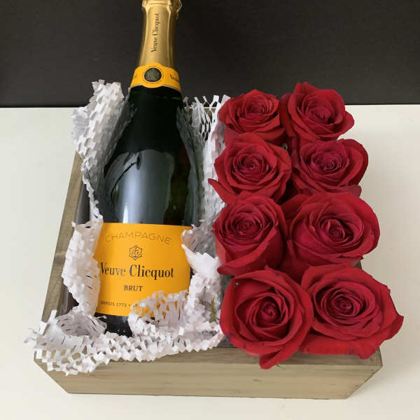 Champagne bottle in a wooden gift box beside red roses