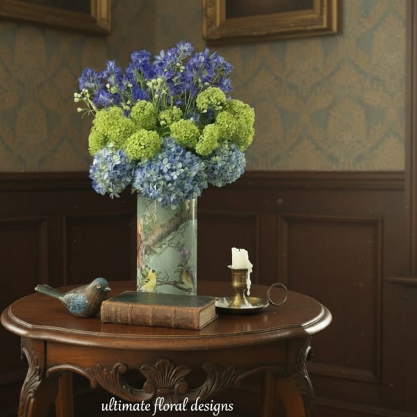 Blue and green hydrangea arrangement in a painted vase on a wooden table