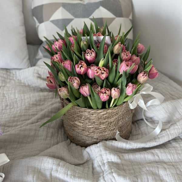 Pink tulips arranged in a woven basket with a white ribbon